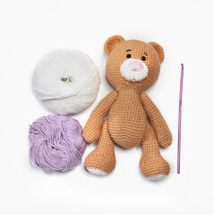 Hand knitted brown bear with a pink nose lying down among balls of thread on white background. Amigurumi