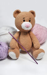 Hand knitted brown bear with a pink nose sitting among balls of thread on white background