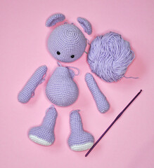 Parts of a knitted purple bear on pink background. Handmade crochet toy. Amigurumi