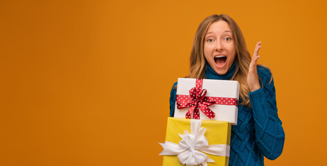 Charming young woman holding a lot of gift boxes. Studio shot, yellow background. New Year, Birthday, Holiday concept