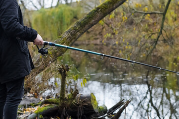 Man fishing in a wild lake. Male hands are holding a fishing rod. Autumn fishing in cold weather.