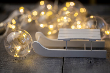 decorative white sledge, illuminated by a garland on a wooden surface