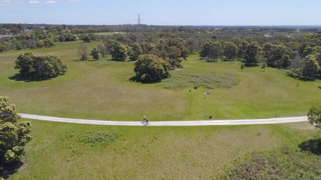 Forward flight over bicycle riders over trees and green grass on bright sunny day in Australia