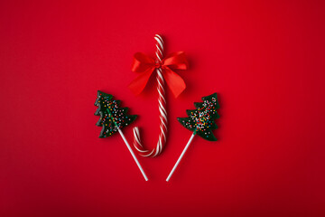 Christmas sweets. Candy Christmas cane with Christmas tree-shaped lollipops on a red background. Lollipops. New Year and Christmas concept. - Powered by Adobe