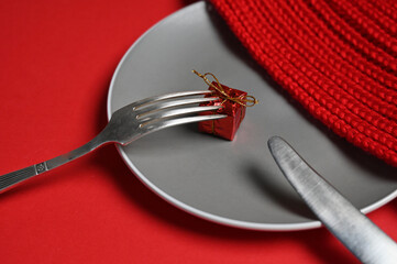Plate with cutlery and gift on red background