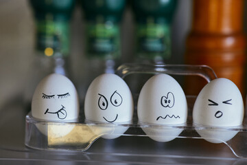 Funny smiling faces on chicken eggs. Four eggs in a box on a blurred background. Types of temperaments. Sanguine, choleric, phlegmatic and melancholic. - obrazy, fototapety, plakaty