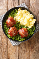 meatballs wrapped in bacon faggot with green peas and mashed potatoes close-up in a plate on the table. vertical top view from above
