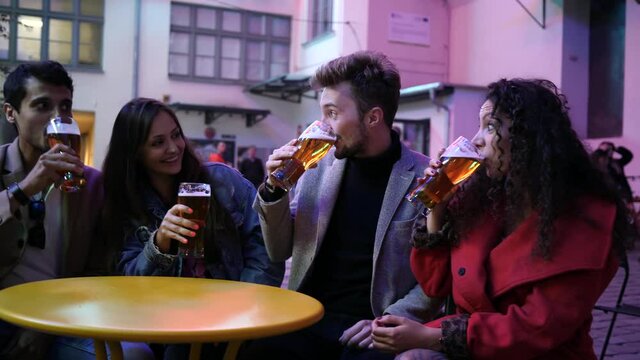 Hang out young people friends drink alcohol beer in city street bar outdoor sit at the table