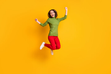 Obraz na płótnie Canvas Full body photo of crazy lady jump high up winner raise fists wear pullover sneakers red trousers isolated yellow color background