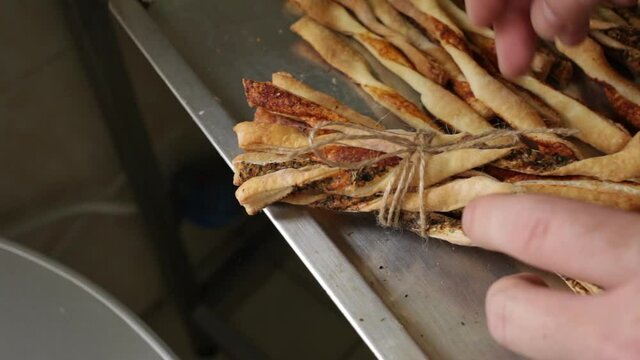The man binds the grissini together with the help of a jute rope. Beautiful breadsticks