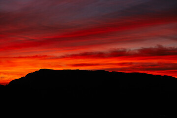 A fiery red sunset over dark mountains. A saturated scarlet sunset and clouds. Sunset sky for Photoshop.