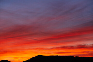 A saturated red sunset. The fiery sky above the silhouette of the mountains. Scarlet autumn sunset clouds.