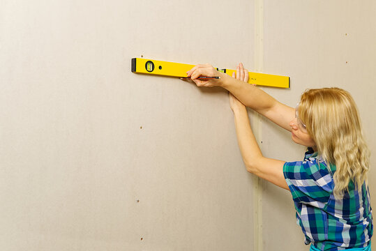 DIY blond young attractive woman using spirit level to work out measurements on plasterboard wall.