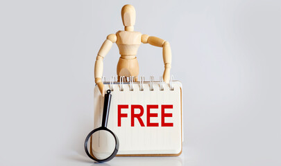 Wooden man shows with a hand to white notepad with text FREE