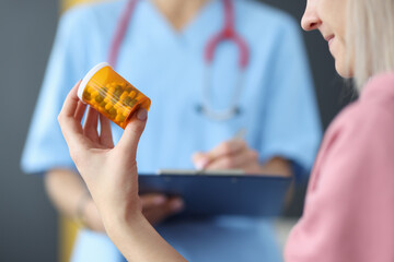 Doctor stands with clipboard next to woman sits and holds pills. Prescribing medicines concept