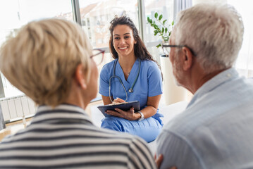 Female nurse talking to seniors patients while being in a home visit, senior couple signs an...