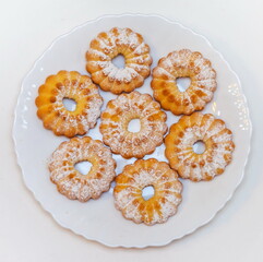 Curly biscuits with icing sugar on white plate closeup on white background