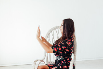 Beautiful fashionable brunette woman sits in a chair with an internet tablet