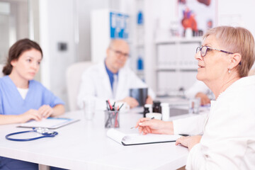 Mature woman doctor explaining diagnosis to medical staff in hospital conference room and having a discussion. Clinic expert therapist talking with colleagues about disease, medicine professional