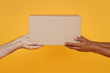 Close up cropped men hold in hands give brown clear blank paper empty cardboard box isolated on yellow background Packaging template mock up Delivery service concept Free Copy space Advertising area.
