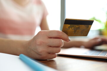 Woman's hand holds credit bank card next to laptop. Online shopping around the world concept