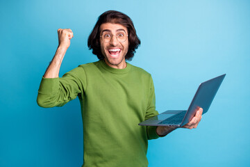 Photo of positive crazy guy hold netbook raise fist open mouth wear eyeglasses green sweater...