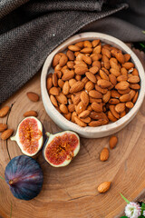 Almonds in a wooden plate next to figs. Nuts and fruits