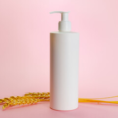 Blank cosmetics container and wheat ears on pink background. Cream or shampoo bottle mockup.