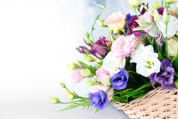 A lush bouquet of multi-colored roses (white, pink, yellow, purple) in a wicker basket stands on a white-gray background. Bright summer bouquet. Holiday concept: women's day, mothers day.