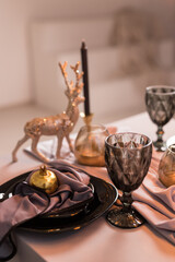 Close up of festive Christmas table setting with empty wine glasses and black plate with gold garnet