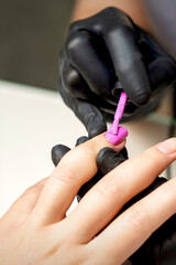 Manicure master applying pink nail polish to female nail in nail salon