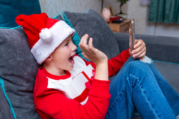 Handsome kid boy in Santa Claus hat looks at smartphone screen. greeting friends,closeup image.