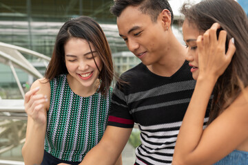 Three young asian friends outdoor in the city looking at something in the boy's hands