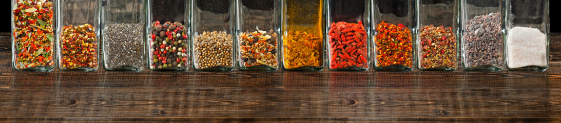 A mixture of various spices in a glass jar close up. Spices and condiments on a black, old shabby board. Free space and copy space for text near condiments.