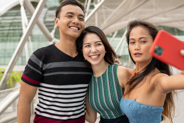 Three asian young friends outdoor taking selfies. City life of two girls and one boy