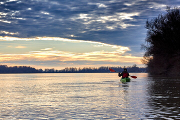 Woman kayaking on green kayak in winter Danube river at sunset. Back view