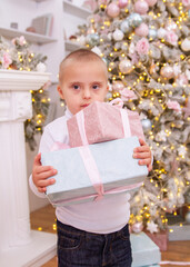 A boy with Down syndrome near the New Year tree, a disabled child holds gift boxes, Christmas gifts...
