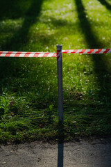 Fototapeta na wymiar A barrier tape separates the natural landscape from the asphalt road. The forest park zone is prohibited. The entrance to the beautiful sunlit lawn in the forest is closed. Respect for nature concept.
