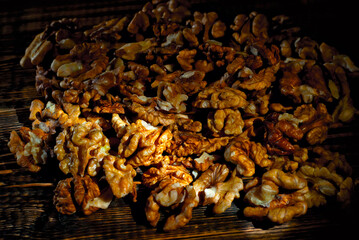 Walnut texture close up. Many halves of peeled nuts on an old wooden board. Food on a background of shabby brown board. Contrasting dramatic light as an artistic effect.