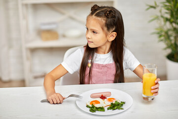 little child girl having breakfast - fried egg and orange juice in the kitchen. healthy breakfast. fried egg face smiles on a white plate