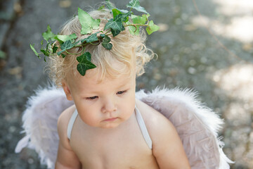 Face of little brooding angel boy with white feather wings in a wreath of live ivy on his head