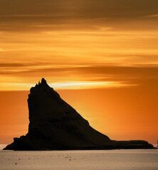 Fototapeta na wymiar Tindholmur boulder peak against orange sky, backlit