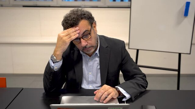 Stressed frustrated businessman wearing glasses at work. Exhausted tensed worker , emotional stress concept feeling pain sitting at office desk with laptop.
