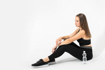 Fototapeta na wymiar Portrait of fitness woman sitting on the floor in sportswear with bottle of water near of her.
