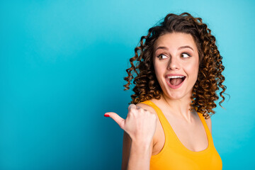 Photo of lovely ginger young lady direct thumb empty space excited look open mouth wear yellow singlet isolated blue color background