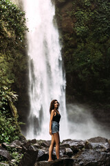 Fototapeta na wymiar Beautiful girl at a waterfall on the island of Bali Indonesia. Sexy woman at the waterfall. Beautiful woman posing at a waterfall. Copy space