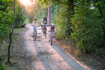 Family riding bicycles in forest at sunset: team, togetherness, wellness