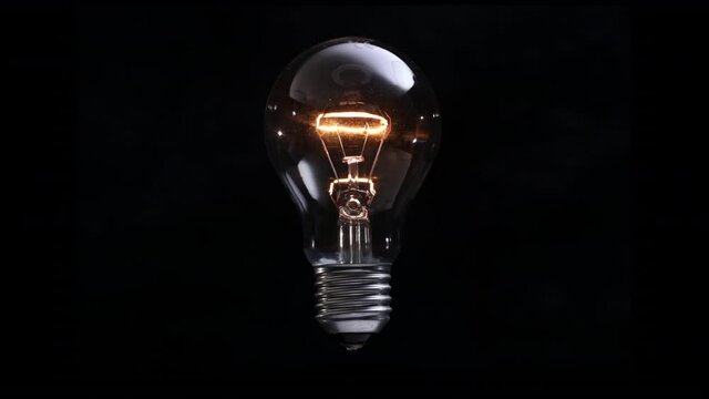 Light bulb hovers and shines slowly on black background. New idea concept. Old type of incandescent light bulb turns on and off.
