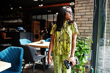 Obraz premium Glamour african american woman wear fashionable snake dress and sunglasses pose at restaurant.