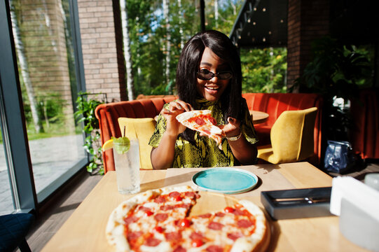 Glamour african american woman eating pizza at restaurant.